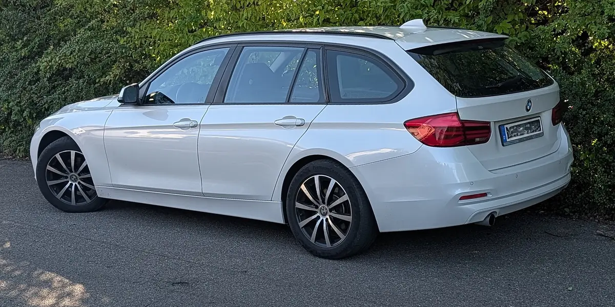 Een witte BMW 3-reeks Touring voor een haag