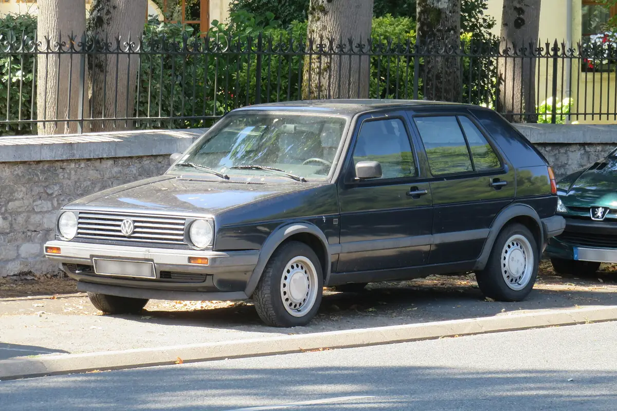 Een donkergrijze Volkswagen Golf II geparkeerd langs een stenen muur